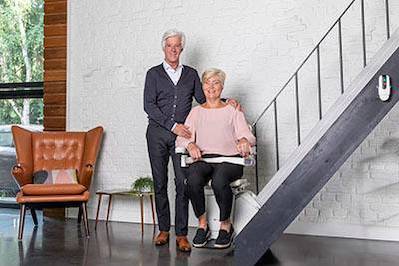 man staat naast vrouw die zit op een traplift
